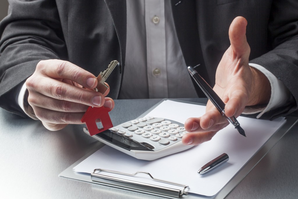 Agent holding house key with contract and calculator