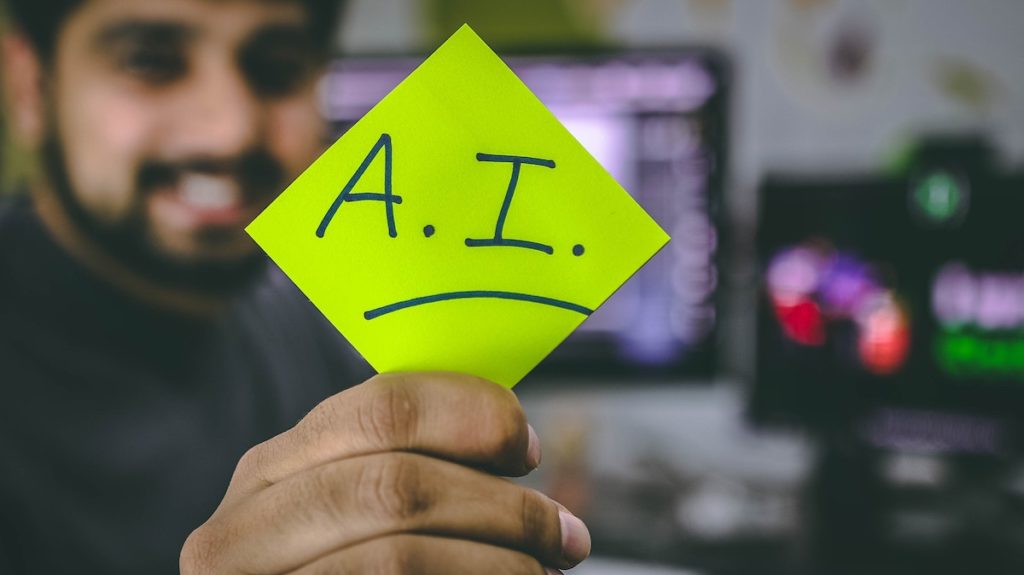man holding out a sticky note with AI written on it