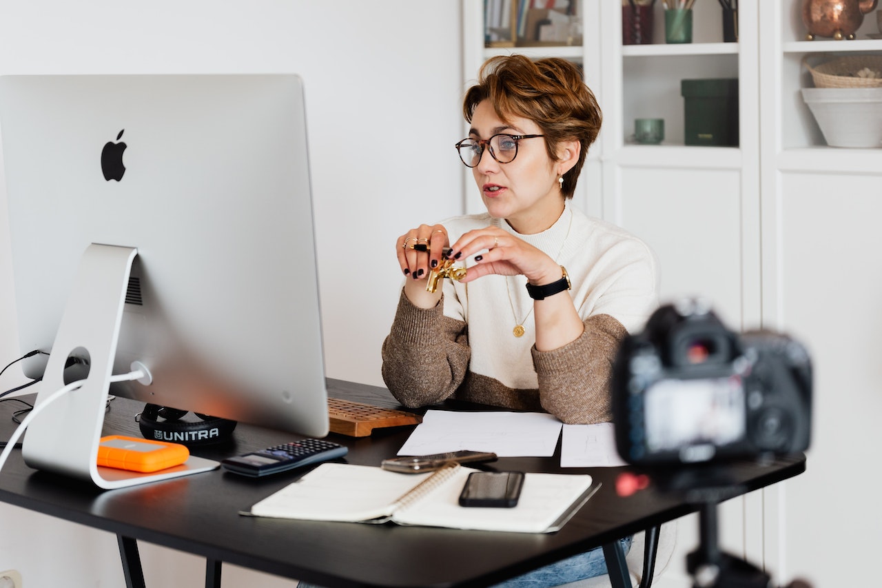 woman with glasses holding up pen and talking to computer screen with camera in foreground